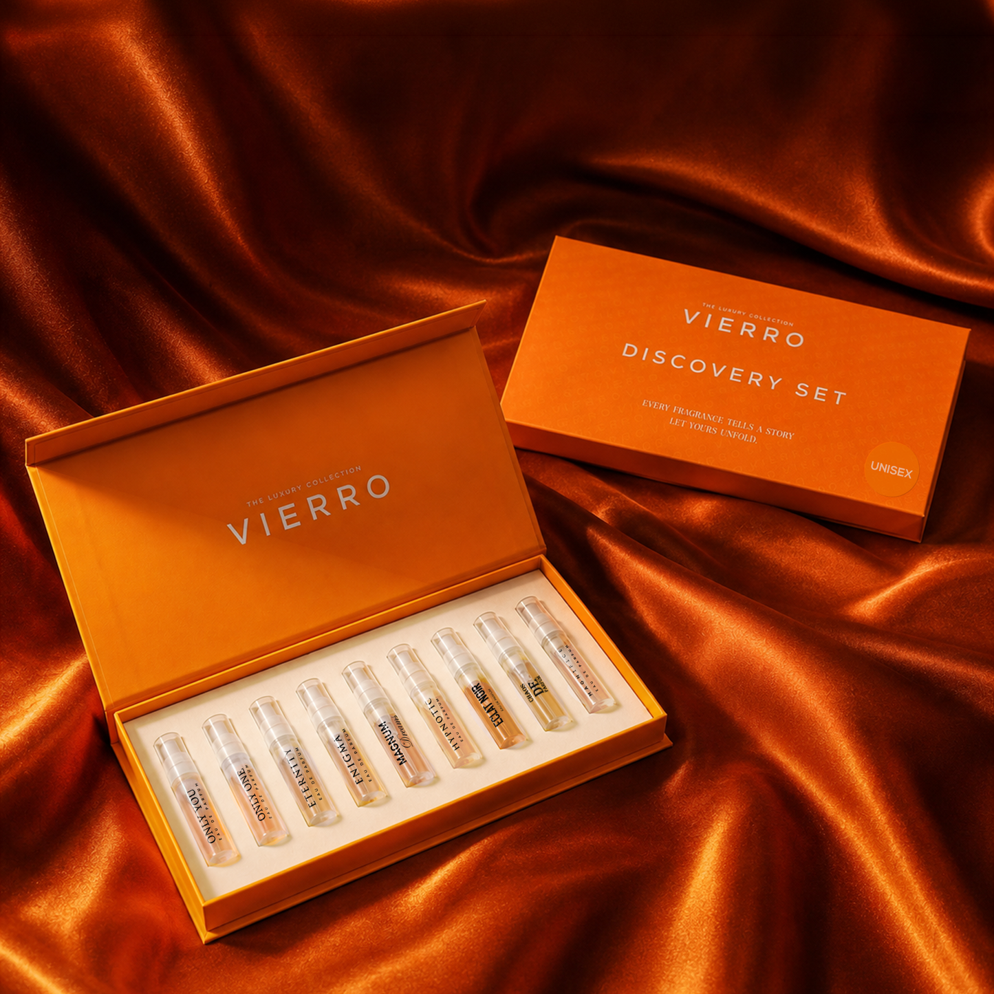 An open orange VIERRO Unisex Discovery Set box with several small clear sample vials inside, placed on draped copper-orange satin fabric beside a matching closed box. 